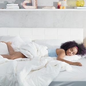 Young African American woman waking up at home. Portrait of happy black girl smiling, enjoying a large king size mattress all for herself.